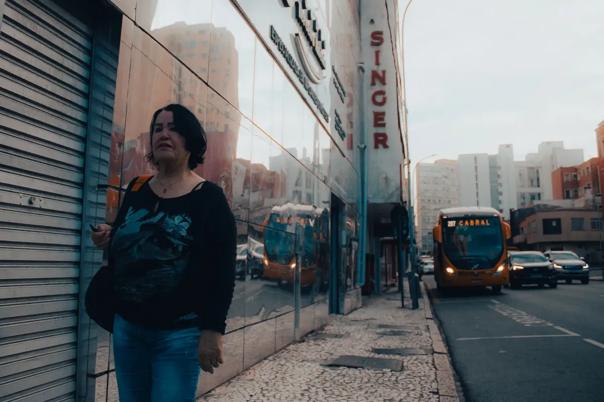 City street in Curitiba, Brazil featuring a woman walking past a bus and cars. Urban life captured.