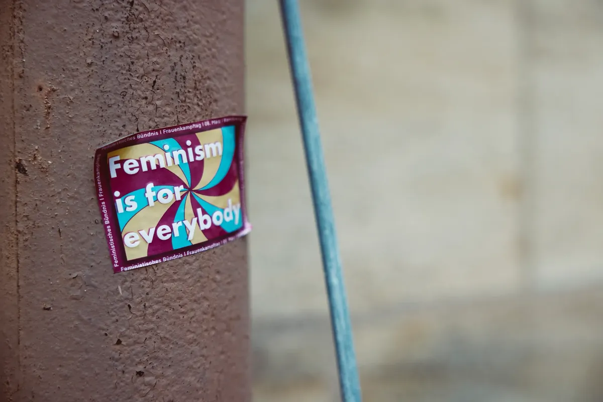 Sticker advocating feminism on pole, promoting equality for all genders.
