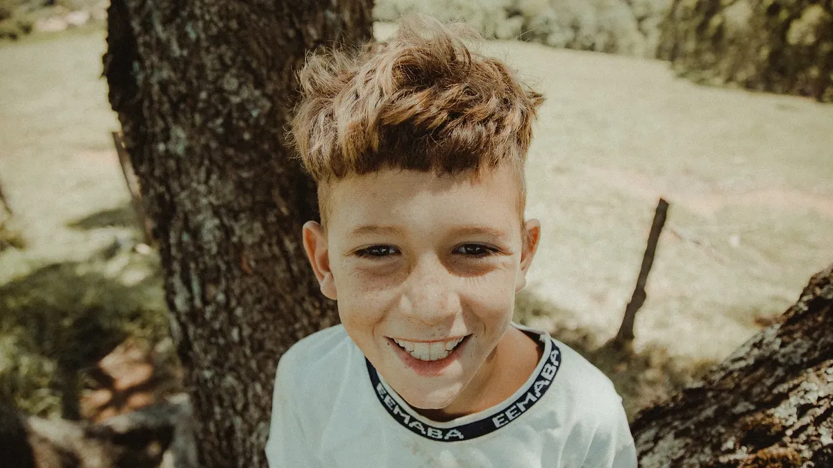 Happy child smiling near a tree in the sunny outdoors of Pedra Bela, Brazil.