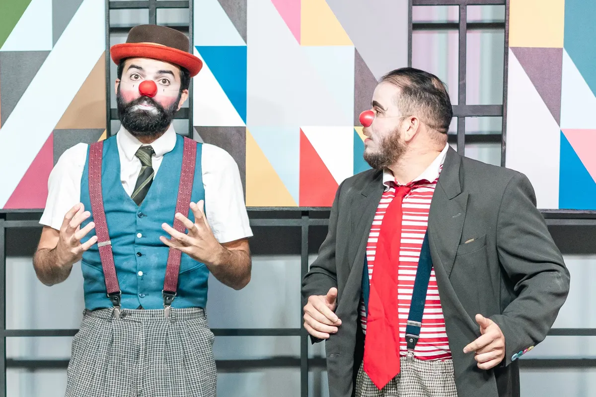 Two clowns in bright costumes performing against a geometric backdrop, showcasing entertainment art.