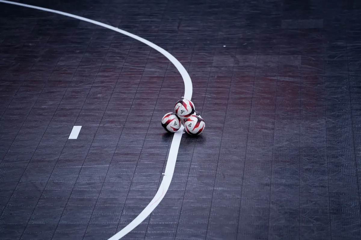 Three soccer balls clustered on a professional indoor sports court with white lines.