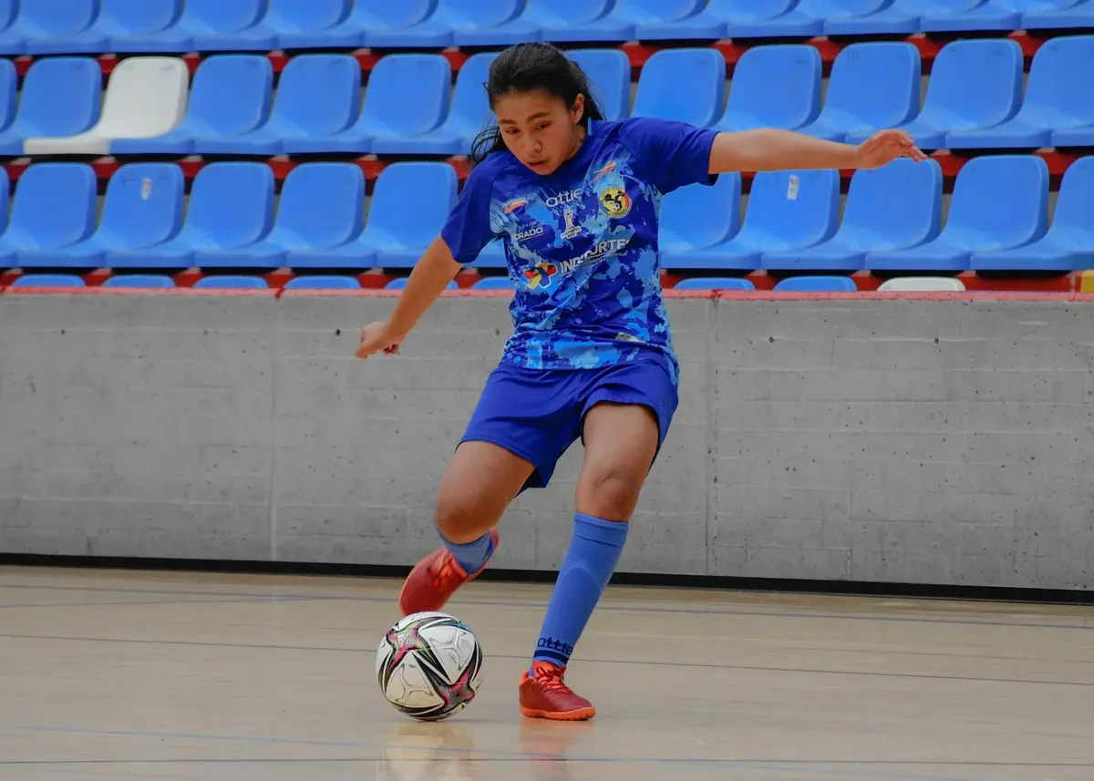 A teenage girl skillfully maneuvers the futsal ball during an indoor match.