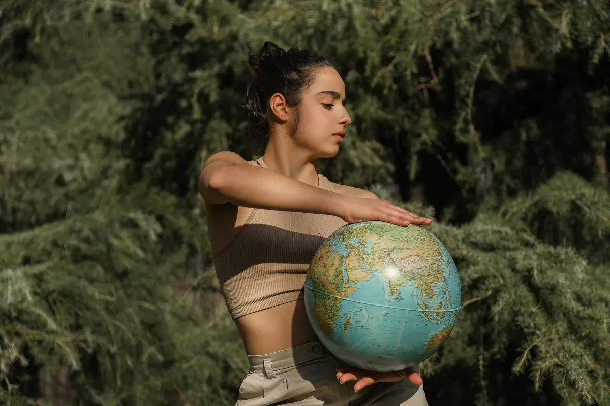 Woman with globe amidst lush greenery, illustrating global awareness and nature connection.