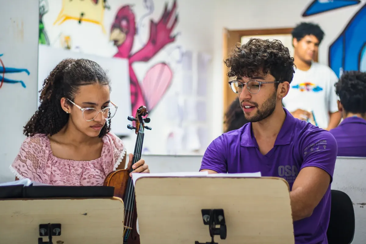 Young man and woman discussing music and violin practice in a colorful classroom.
